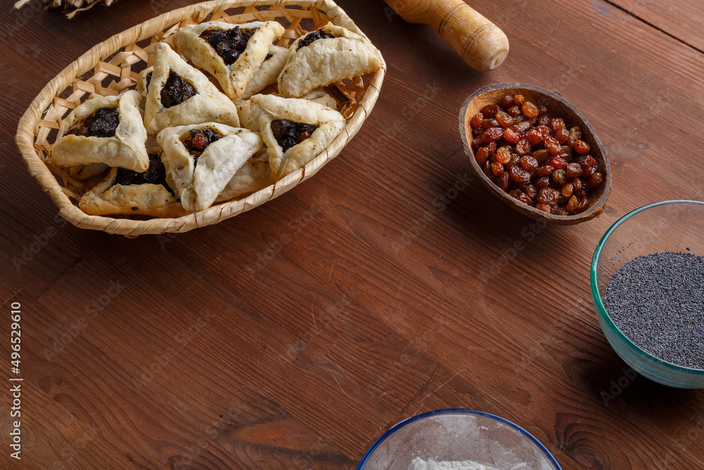 Fototapeta premium Gomentash with poppy seeds and prunes freshly baked for Purim holiday on a wooden table in a wicker bread basket near poppy seeds and raisins.copy space.