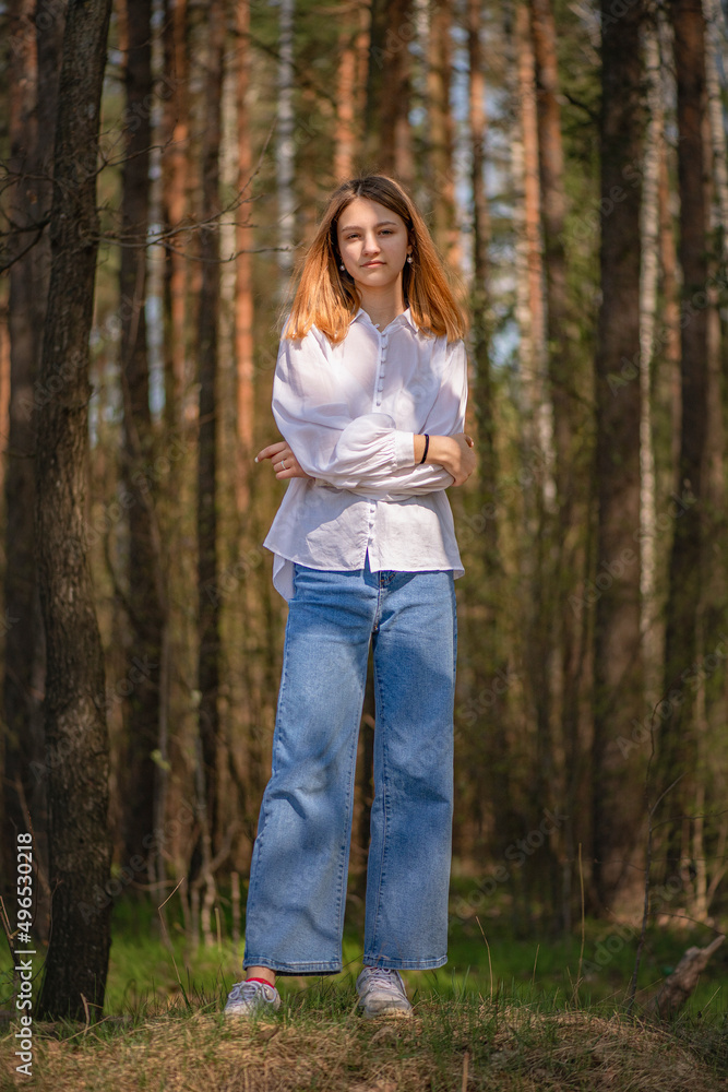 Portrait of a young beautiful blonde girl in jeans and a white shirt in a summer forest. Portrait of a young beautiful blonde girl in jeans and a white shirt in a summer forest.