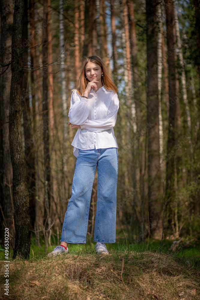 Portrait of a young beautiful blonde girl in jeans and a white shirt in a summer forest. Portrait of a young beautiful blonde girl in jeans and a white shirt in a summer forest.