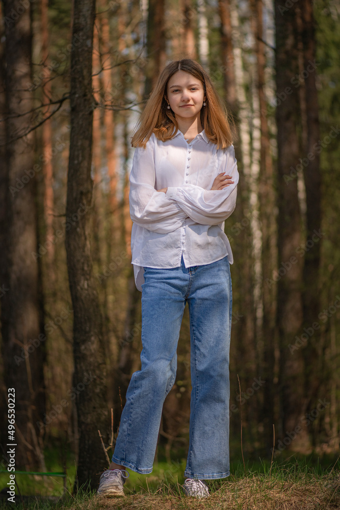 Portrait of a young beautiful blonde girl in jeans and a white shirt in a summer forest. Portrait of a young beautiful blonde girl in jeans and a white shirt in a summer forest.