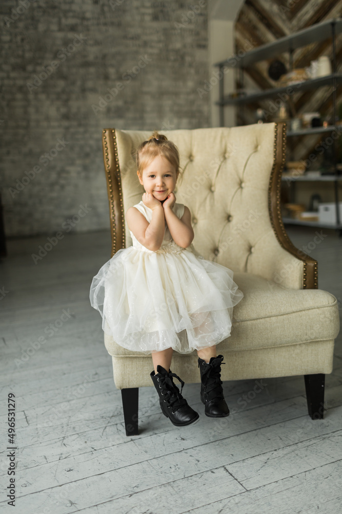 .a little girl sits on a beautiful armchair in a photo studio