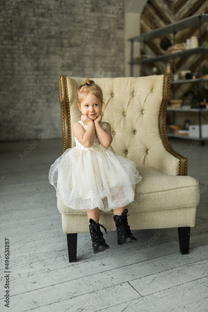 .a little girl sits on a beautiful armchair in a photo studio