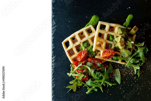 Fresh baked Belgian waffles with arugula, tomatoes and avocado on black a plate isolated on white background. Savory waffles. Breakfast concept. Healthy breakfast