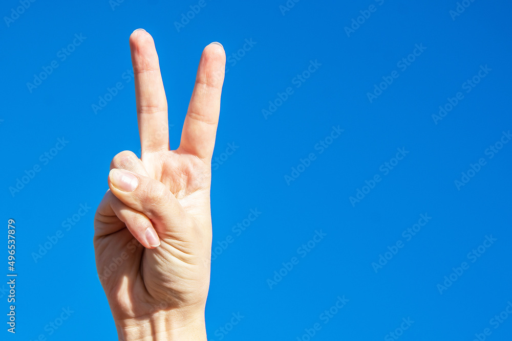 Symbol of peace. Raised fingers up. Palm on a background of blue sky Symbol of peace. Raised fingers up. Palm on a background of blue sky