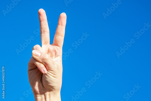 Symbol of peace. Raised fingers up. Palm on a background of blue sky