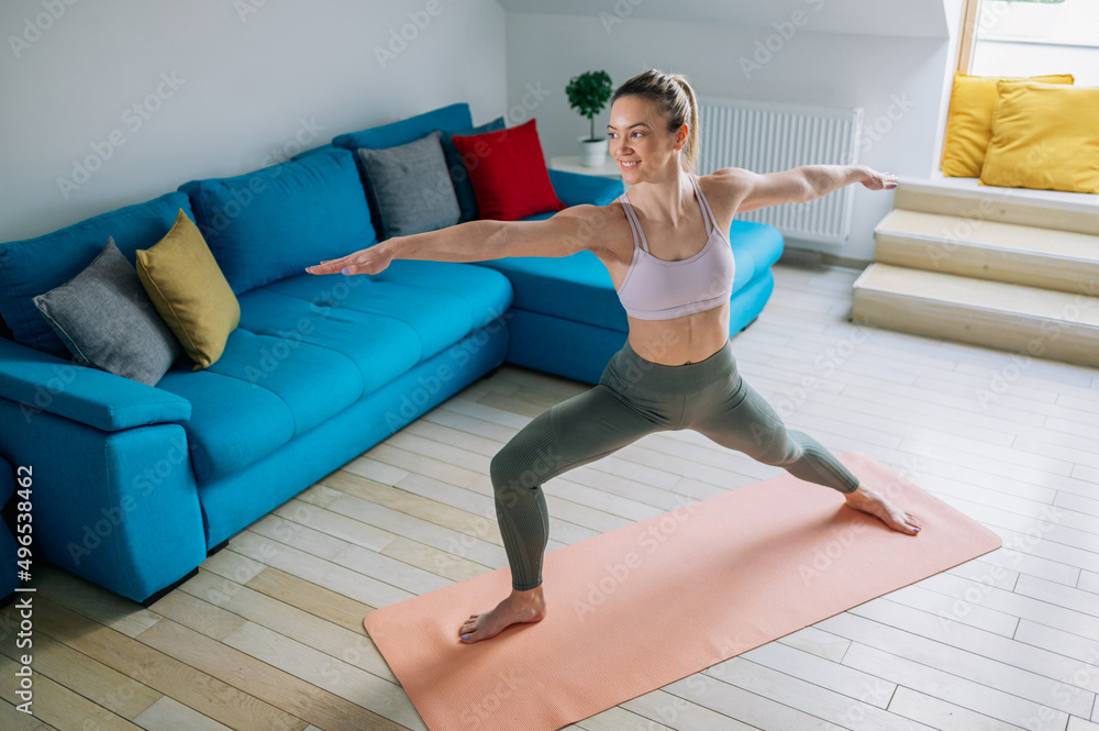 Fototapeta premium Woman training yoga at home an standing in Warrior Two pose.