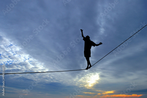 Silhouette of young man balancing on slackline, sun and clouds behind. Slackliner balancing on tightrope between two rocks, highline silhouette. photo