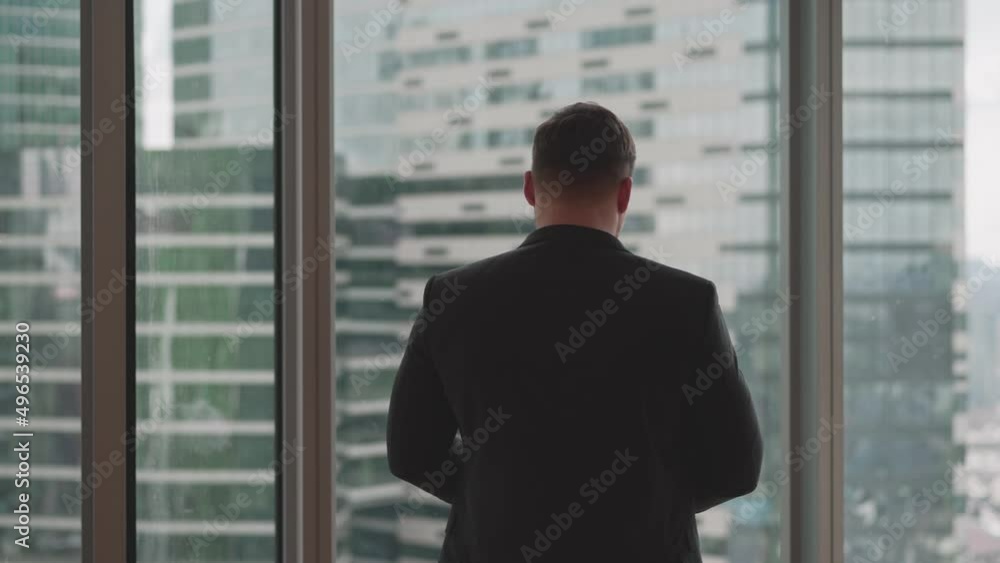 A businessman stands by the window against the backdrop of skyscrapers. A young promising businessman in a suit stands against the background of the panoramic windows of his office. A businessman A businessman stands by the window against the backdrop of skyscrapers. A young promising businessman in a suit stands against the background of the panoramic windows of his office. A businessman