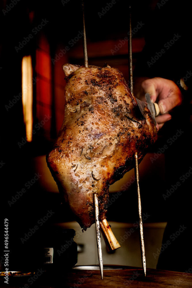 man cutting lamb shank roasted in barbecue on wooden board StockFoto