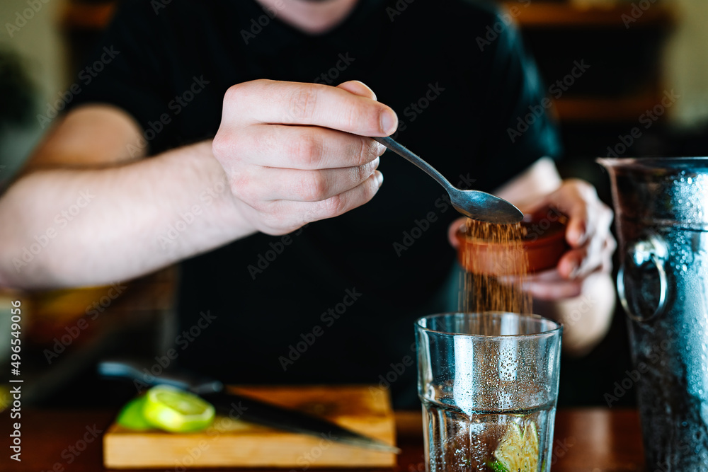 hands of a young waiter, adding brown sugar in a large crystal glass to prepare a Mojito. horizontal. hands of a young waiter, adding brown sugar in a large crystal glass to prepare a Mojito. horizontal.