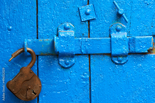 An old wood blue painted door with metal rusted latch, padlock and antique door handle