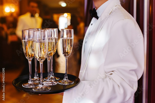 Side view of faceless waiter in uniform, carrying tray with glasses of champagne during wedding party against blurred background