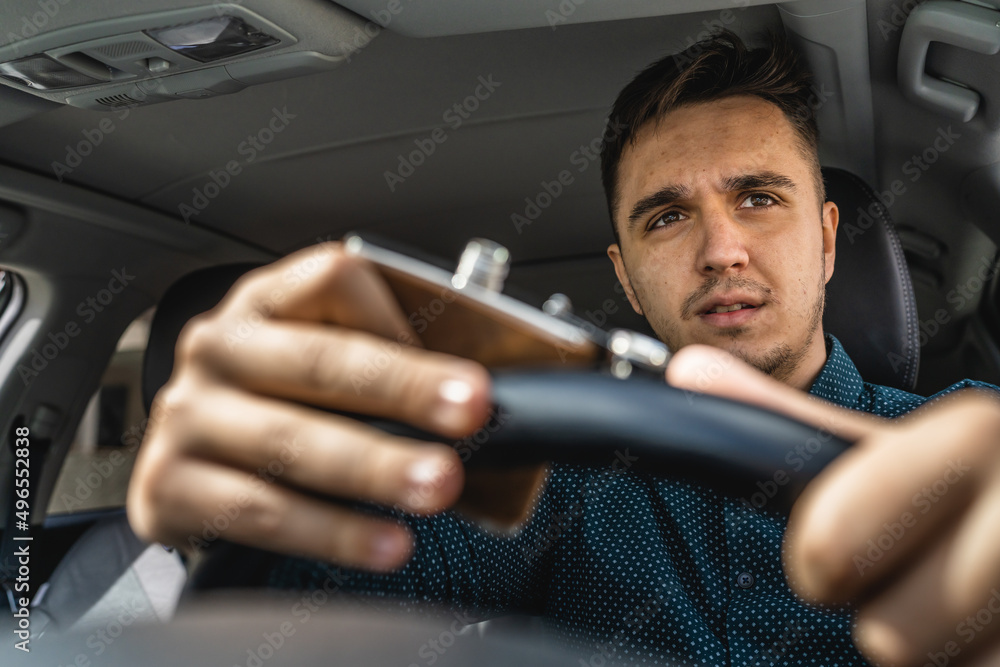 One man caucasian male drinking alcohol from flask while drive a car drunk close up on drink alcoholism and alcohol abuse concept intoxicated dangerous nervous driver hands on the steering wheel One man caucasian male drinking alcohol from flask while drive a car drunk close up on drink alcoholism and alcohol abuse concept intoxicated dangerous nervous driver hands on the steering wheel