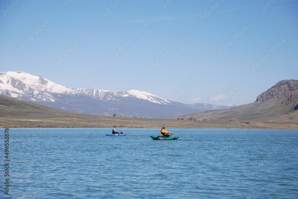 A pair of anglers fishing from pontoons on a mountain lake. A pair of anglers fishing from pontoons on a mountain lake.