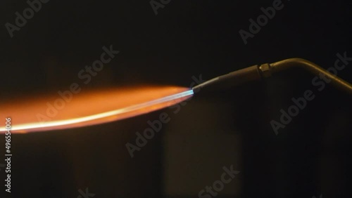 Close-up of the end of a blowtorch with a gas fire igniting orange flame. The flame of a blowtorch on the background of the workshop. Butane gas burner flame burning. Slow motion. High speed camera 4K photo