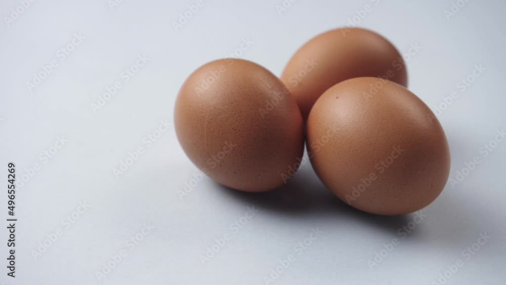 Eggs rotate on white background. Close-up of three fresh, organic and healthy chicken egg. Brown Eggs are rolling on the white table. Easter eggs clean background. Eggs rotate on white background. Close-up of three fresh, organic and healthy chicken egg. Brown Eggs are rolling on the white table. Easter eggs clean background.