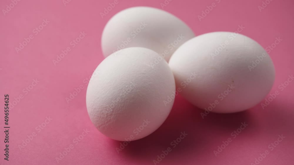 Eggs rotate on pink background. Close-up of three fresh, organic and healthy chicken egg. White Eggs are rolling on the clean pink table. Easter eggs background. Eggs rotate on pink background. Close-up of three fresh, organic and healthy chicken egg. White Eggs are rolling on the clean pink table. Easter eggs background.
