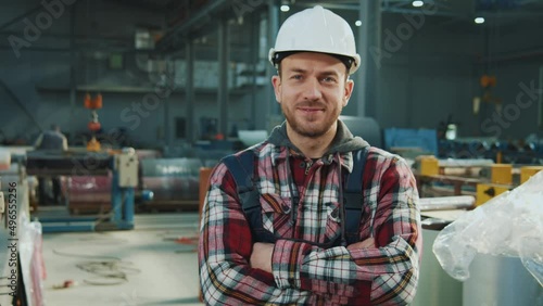 Handsome industry engineer man wears safety uniform and hard hat stand look at camera smiling feel happy in factory. Inspector in warehouse.