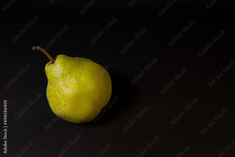 Ripe green pear on a dark background, late November pear variety. Whole fruit Ripe green pear on a dark background, late November pear variety. Whole fruit