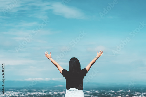 Woman raise hand up at top of rock on blue sky and white cloud abstract background. Freedom feel good and travel adventure vacation concept.