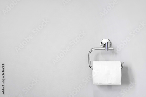 Chrome toilet paper holder on white wall holding a roll of soft bath tissue. Design element and copy space. photo