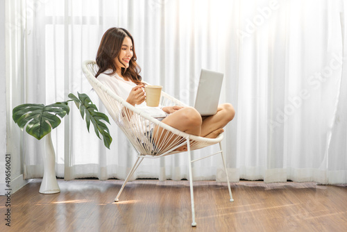 Young smiling happy beautiful asian woman relaxing using laptop computer in the bedroom at home.Young creative girl working and typing on keyboard.work from home concept