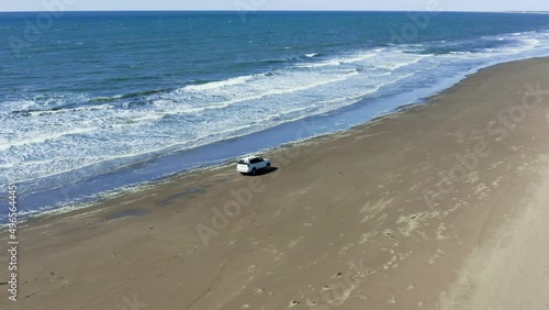 The car moves on a summer day along the sandy sea beach, crosses the rivers and white foam from the waves. 