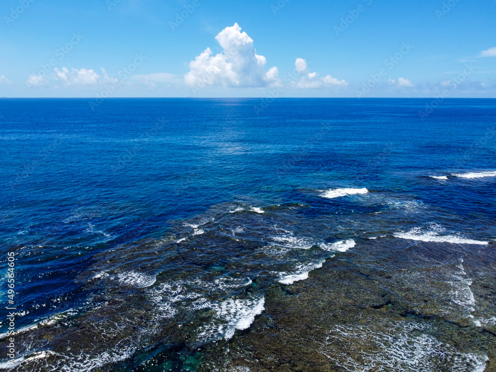 晴れた日の沖縄の青い海と珊瑚礁と波と水平線と入道雲