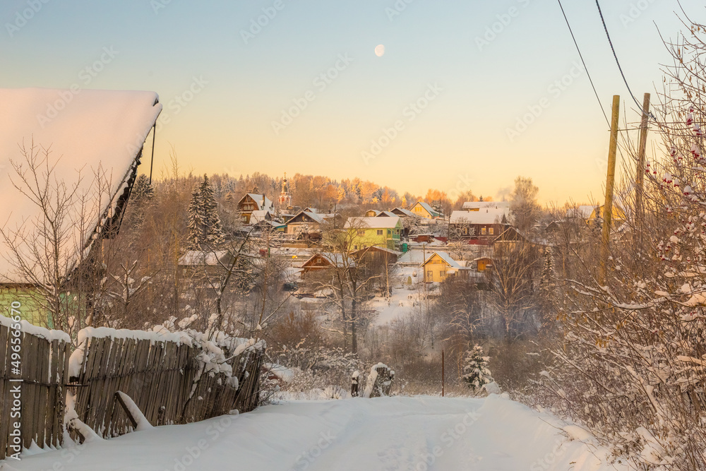 a full moon hangs in a clear sky over a snow-covered village perched on a steep slope on a frosty winter morning