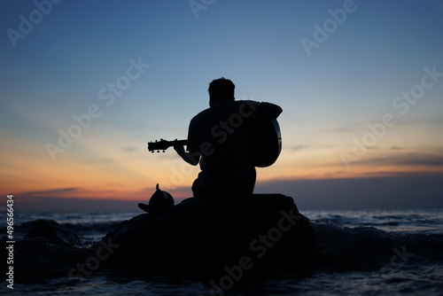 A man playing guitar on rocks with the silhouette.