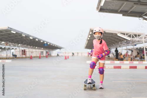 asian child or kid girl playing surf skate or skateboard in skating rink or sport public park at parking to wearing face mask helmet with elbow pads wrist and knee support for body safety to protect