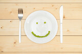 The concept of healthy eating, green peas laid out on a white plate in the shape of a smile. Top view