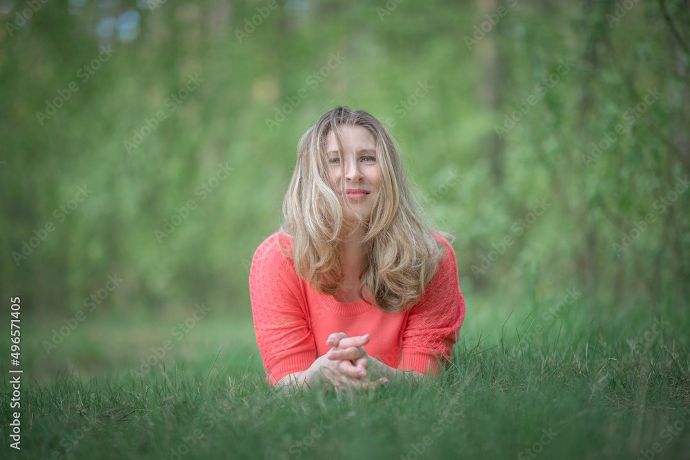 Fototapeta premium Beautiful blonde young woman in a pink blouse in the park.