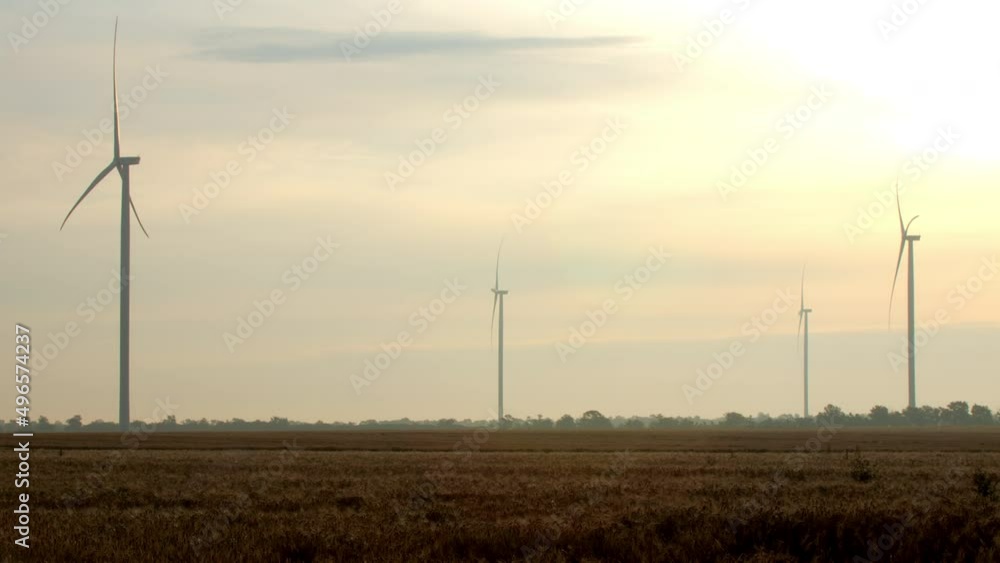 Wind generators produce renewable power at eco-friendly station in countryside. Large propellers rotate in field against cloudy sky at sunrise Wind generators produce renewable power at eco-friendly station in countryside. Large propellers rotate in field against cloudy sky at sunrise