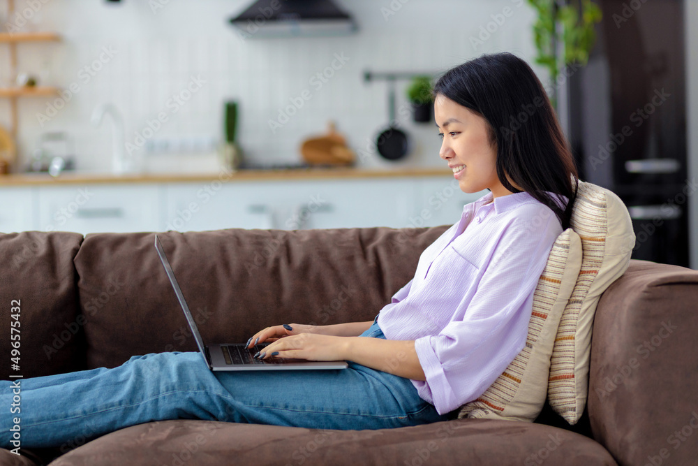 Happy Asian woman using laptop on sitting of cozy sofa at home chatting on social network or looking for something on the Internet Happy Asian woman using laptop on sitting of cozy sofa at home chatting on social network or looking for something on the Internet