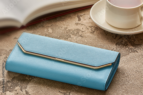 A blue woman's purse lies on a concrete background with a cup of coffee and a book photo