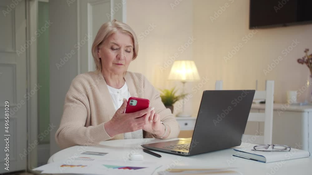 An elderly woman sits at a table and learns to use the phone on her own An elderly woman sits at a table and learns to use the phone on her own