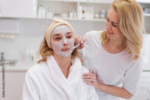 Cosmetology. Professional beautician in medical mask and rubber gloves applies a mask to the client s face. The concept of professional help in beauty salons during a pandemic.