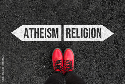 Photos woman with boots are standing on asphalt next to arrow signs of words atheism an