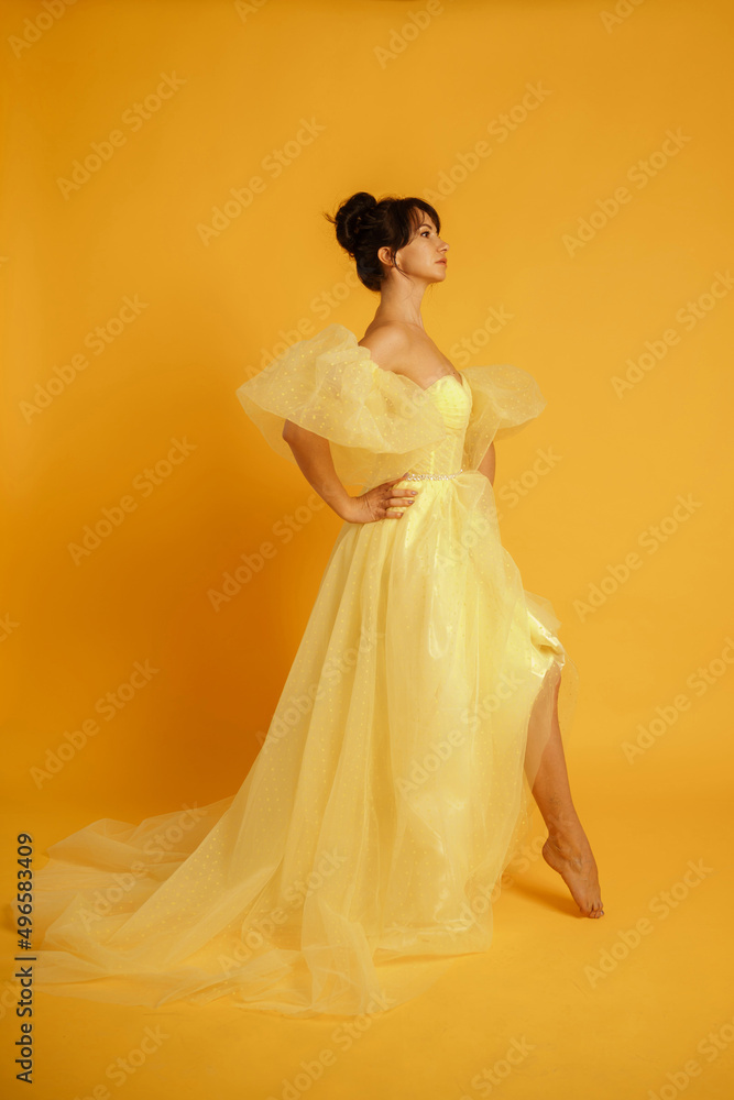 Fototapeta premium Profile portrait of a beautiful middle-aged woman in a yellow dress, her hair pulled up against a yellow background