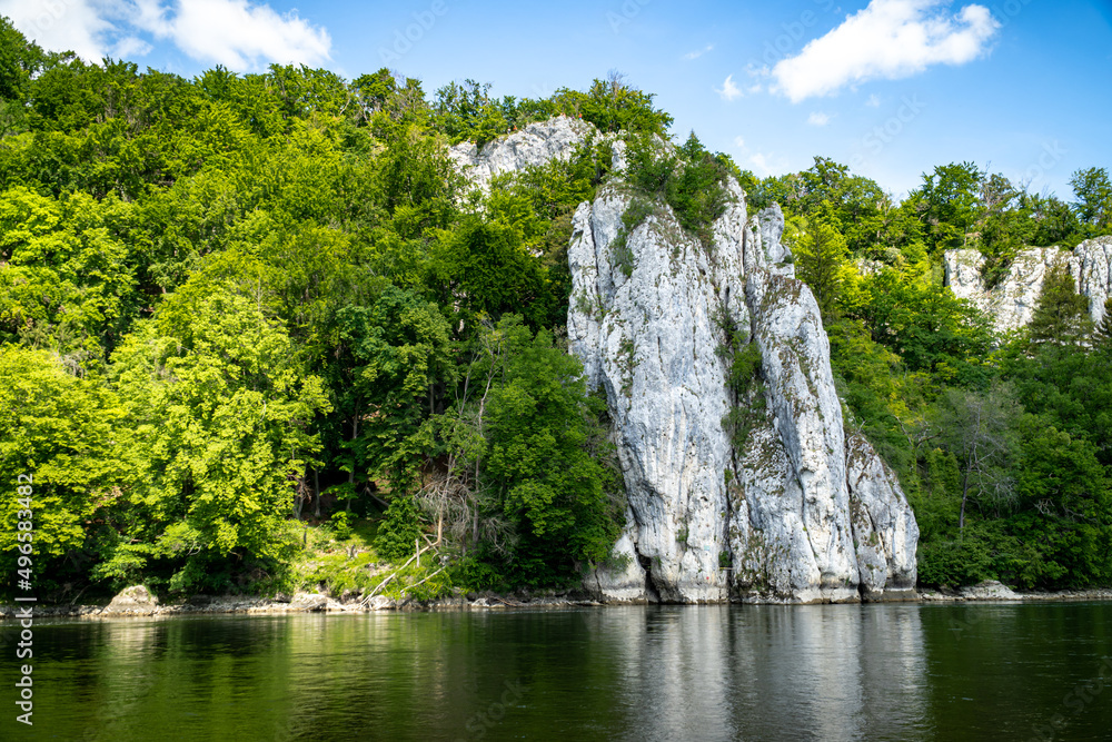 Rocks of the Danube Gorge with green forest, blue sky, water and beach of the Danube. Danube Gorge in Bavaria Germany.