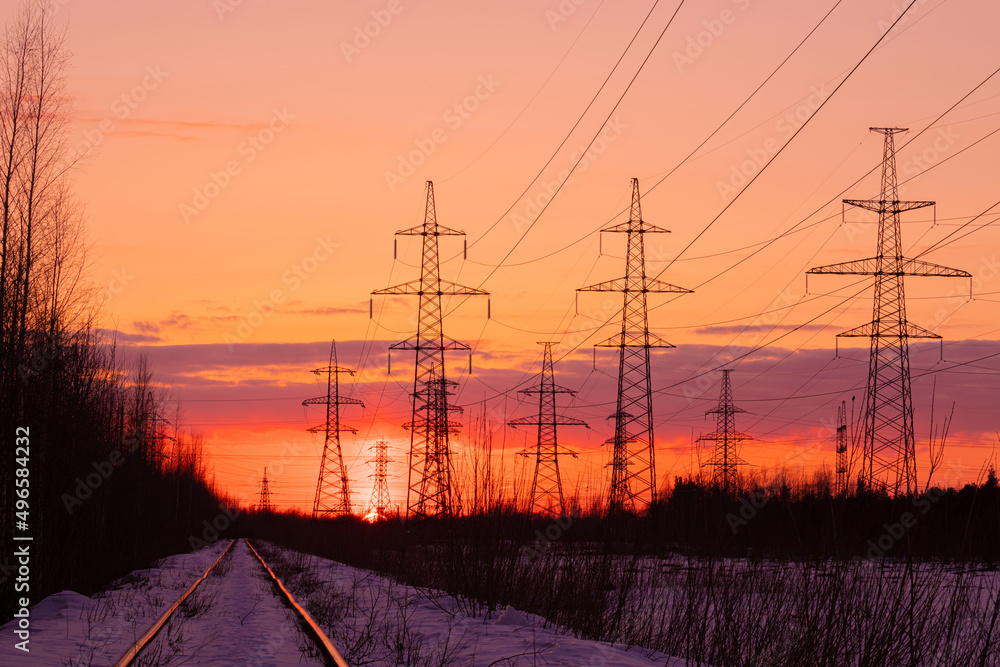 The towers of electric main in the countryside near old railway on the background red, orange and yellow sunset or sunrise sky