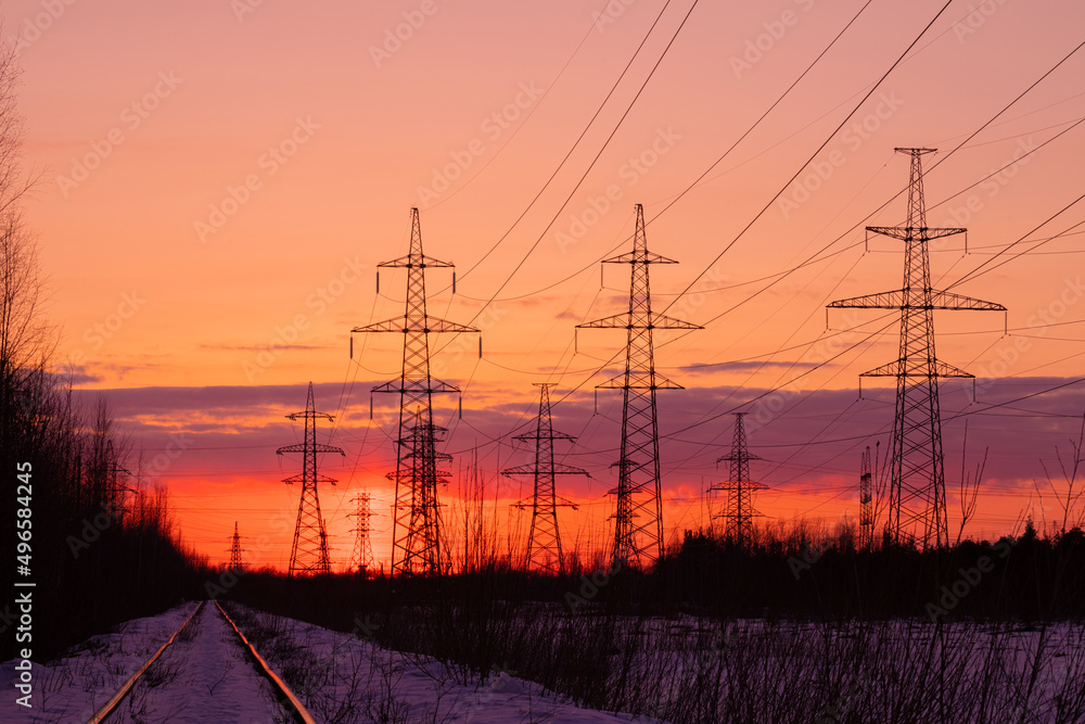 The towers of electric main in the countryside near old railway on the background red, orange and yellow sunset or sunrise sky