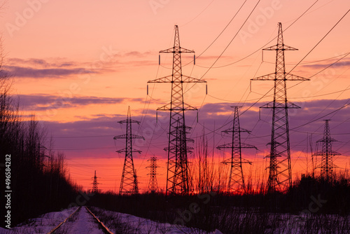 The towers of electric main in the countryside near old railway on the background red, orange and yellow sunset or sunrise sky