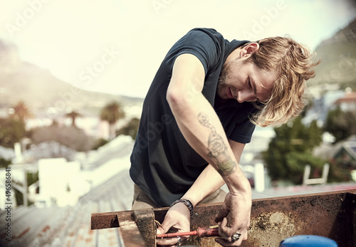 Getting some repairs done. Cropped shot of a handsome young man working outside on his roof.