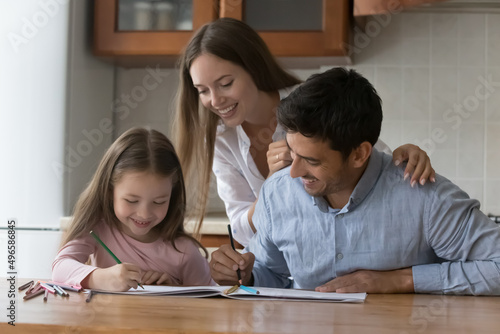Happy parents and little daughter kid drawing colorful doodles in paper albums at kitchen table , having fun, talking, laughing, using colored pencils, enjoying family creative hobby