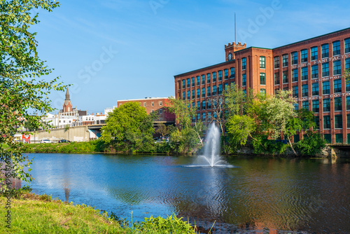 Fountain on the Nashua River against the background of a historic cotton factory building with a clock tower in the old industrial park of Nashua. New Hampshire, USA