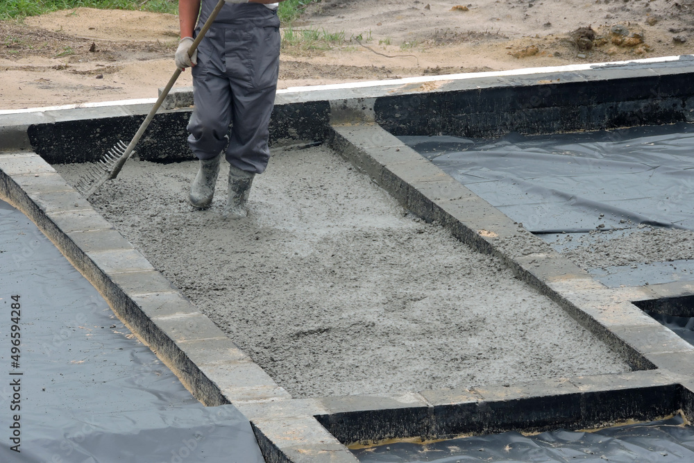 A builder levelling and spreading concrete with a rake A builder levelling and spreading concrete with a rake