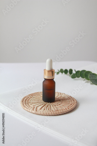 Dropper bottle serum on wood plate. Natural facial essential oil or serum packaging on white fabric background. Beauty product branding mock-up. Cosmetic skincare concept. 