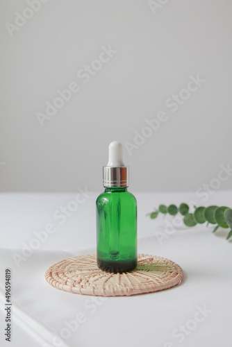Dropper bottle serum on wood plate. Natural facial essential oil or serum packaging on white fabric background. Beauty product branding mock-up.  Cosmetic skincare concept. 